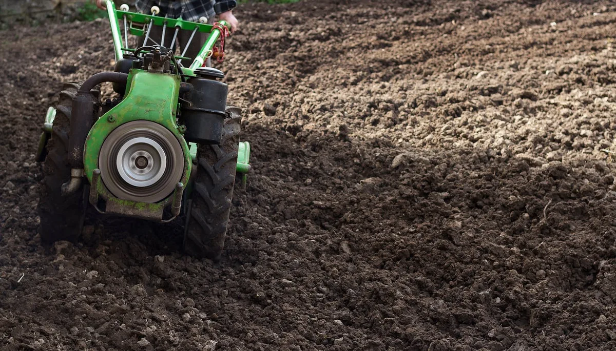 Farmer using small tractor cultivating and tilling soil in field before planting