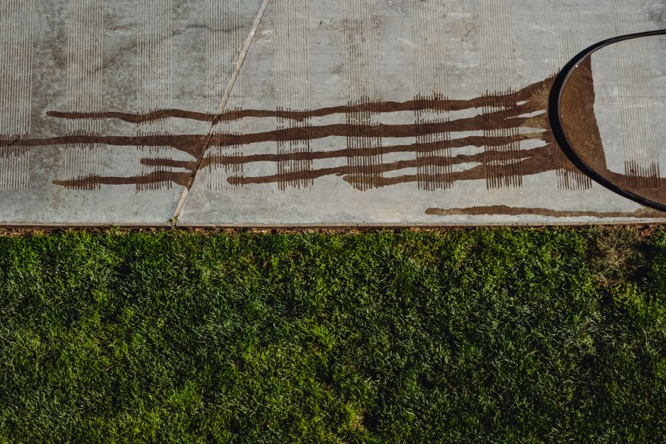 Overhead view of green lawn meeting a concrete driveway with soil washed across the concrete