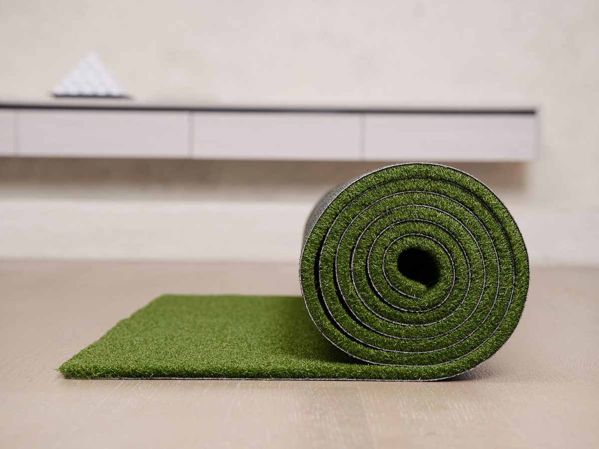 Roll of synthetic artificial grass partly unrolled on a floor showing its green plastic blades